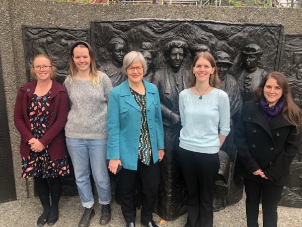 Minister Sage poses with four young people to announce the Suffrage 125 fund recipients. They are standing in front of a sculpture of famous suffragists such as Kate Sheppard.
