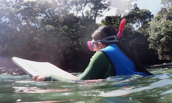 Girl swims outdoors with floating board and snorkel. 