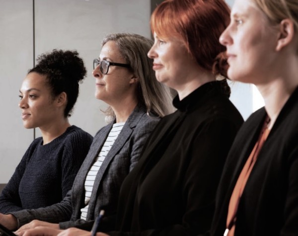 Four women sit in a line at a board meeting