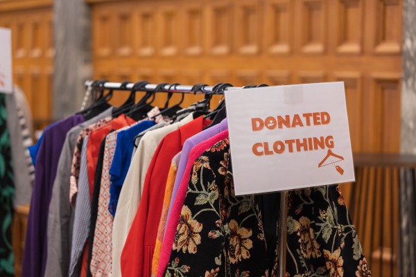 Range of women's clothes in different colours hang on a rack with a sign saying "Donated clothing"