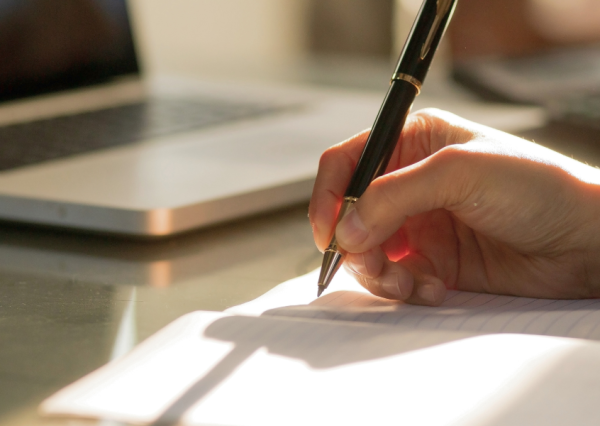 Hand holds pen over piece of paper to start writing