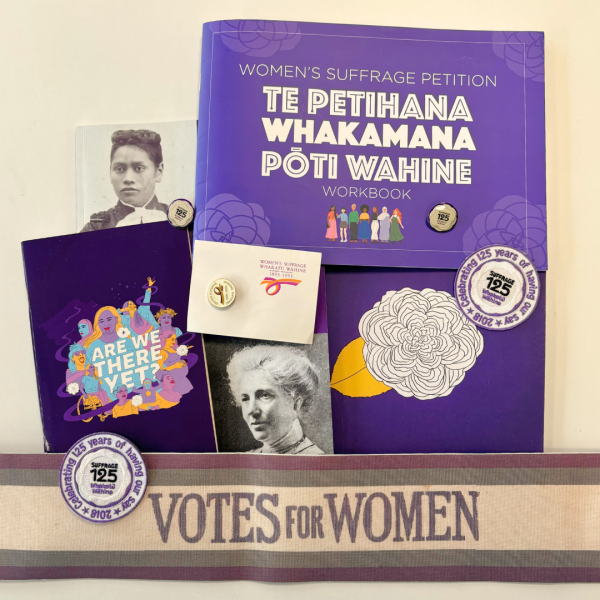 A collection of purple books and badges all celebrating suffrage day. Pictures include a white flower, suffrage 125, and old black and white portraits of two women.There is a sash saying "votes for women" at the bottom.