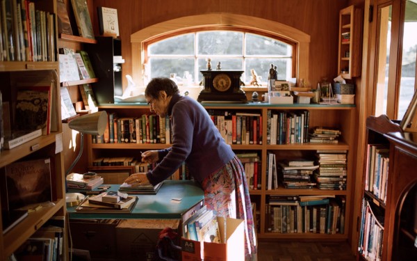 Older woman stands over a table indoors in a room full of books