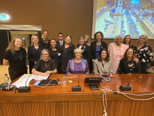 A large group of people stand together and smile behind a wooden desk.