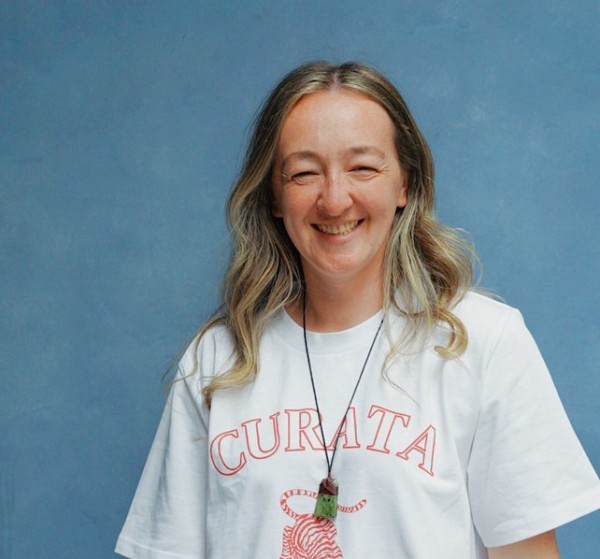 Blond woman in white shirt smiles in front of a blue background 